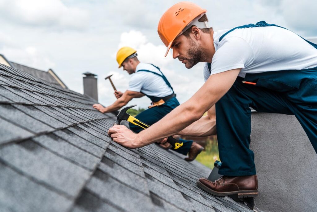 roofing contractors hammer shingles onto new roof